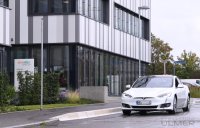 Tesla Fan im Auto vor dem Hauptgebaeude des Biopharma-Unternehmen Curevac